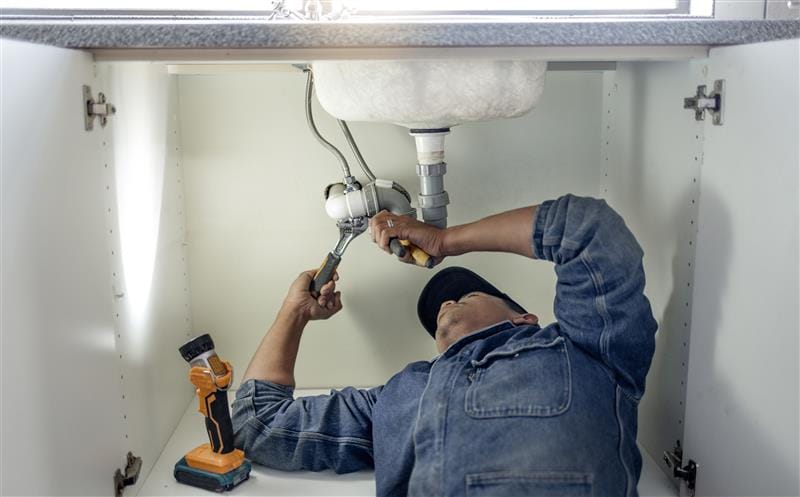 Plumber repairing pipes beneath a bathroom sink in Edgewater