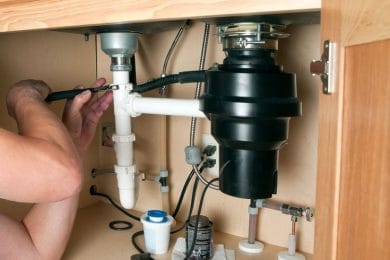 Plumber repairing a garbage disposal beneath a kitchen sink in Edgewater