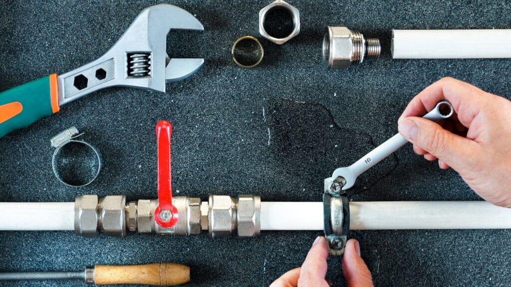 Plumber repairing a pipe valve with an adjustable wrench in Edgewater