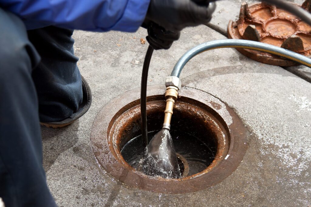 Plumber hydro jetting a sewer line through a manhole in Edgewater