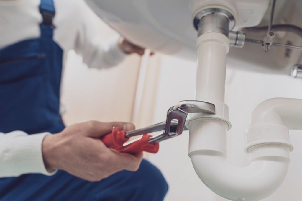 Plumber repairing a white drain pipe beneath a sink in Edgewater