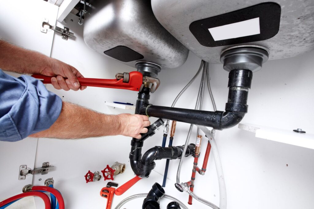Plumber repairing drain pipes beneath a kitchen sink in Edgewater